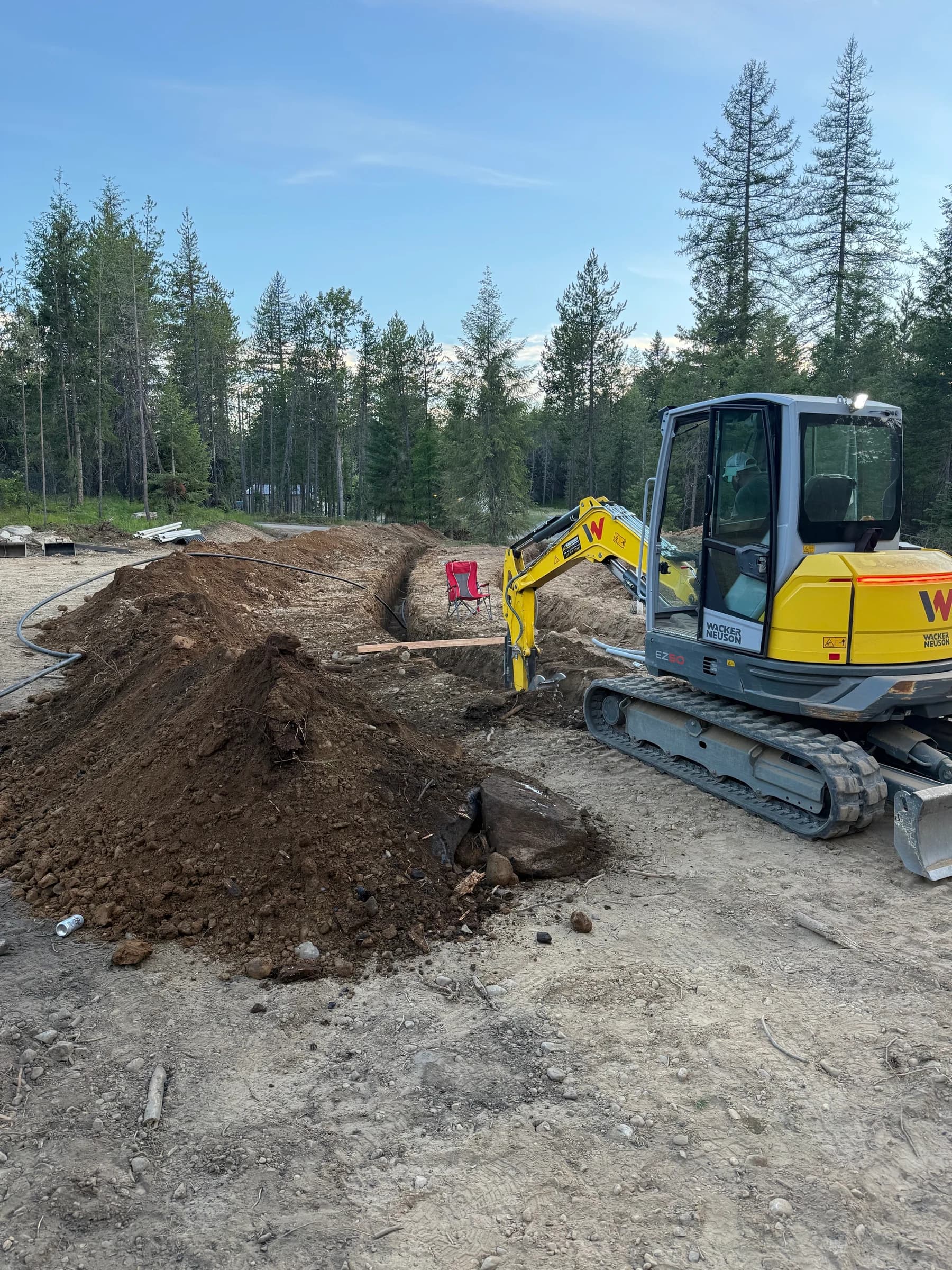 Yellow compact excavator beside an open trench and piles of excavated soil