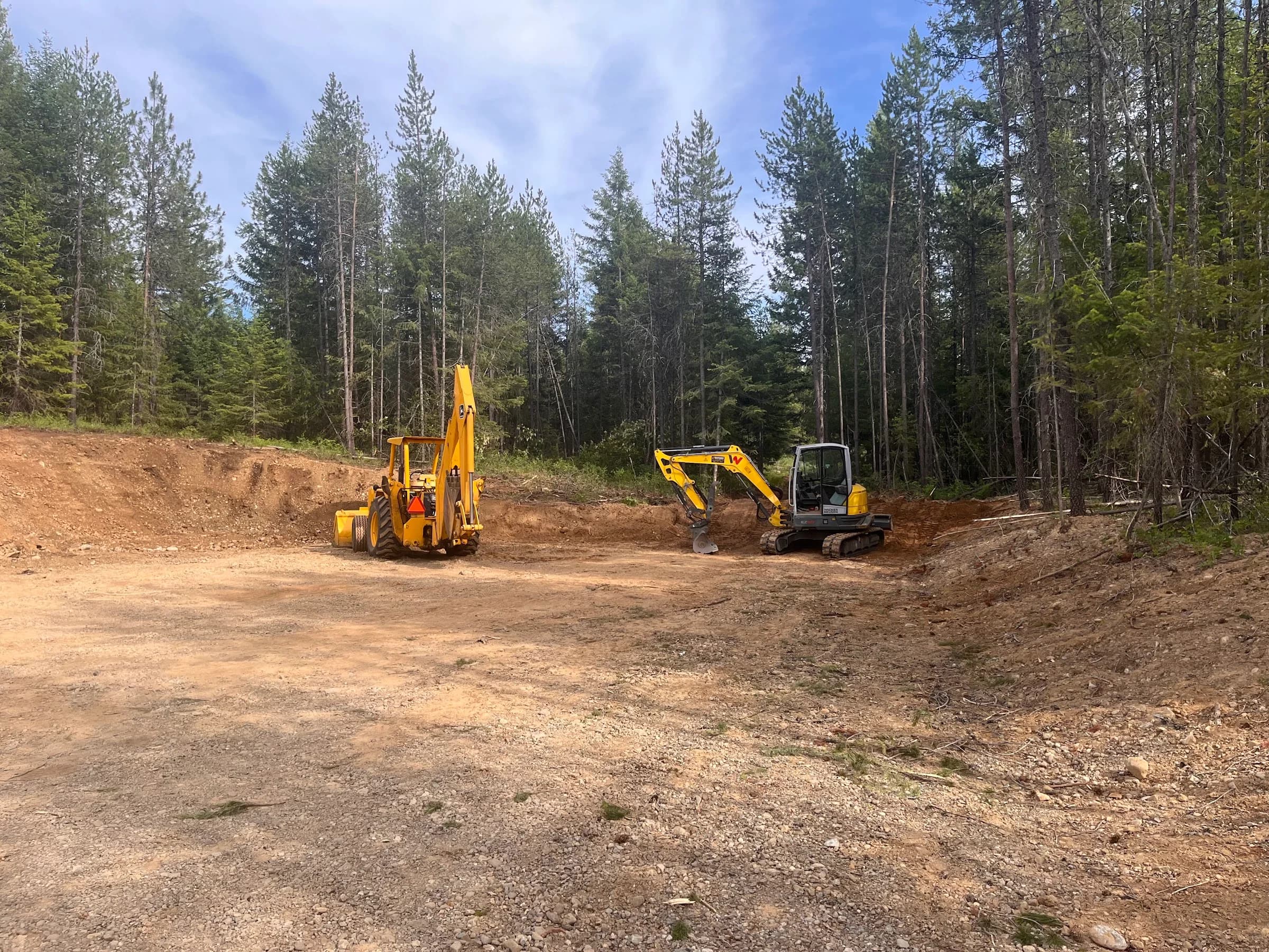 Two yellow earthmoving machines at a wooded work site