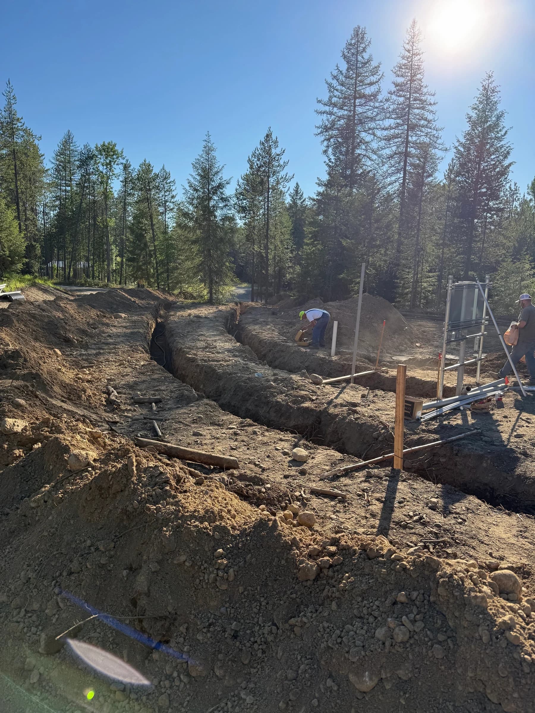 People working beside open trenches and equipment at a wooded site