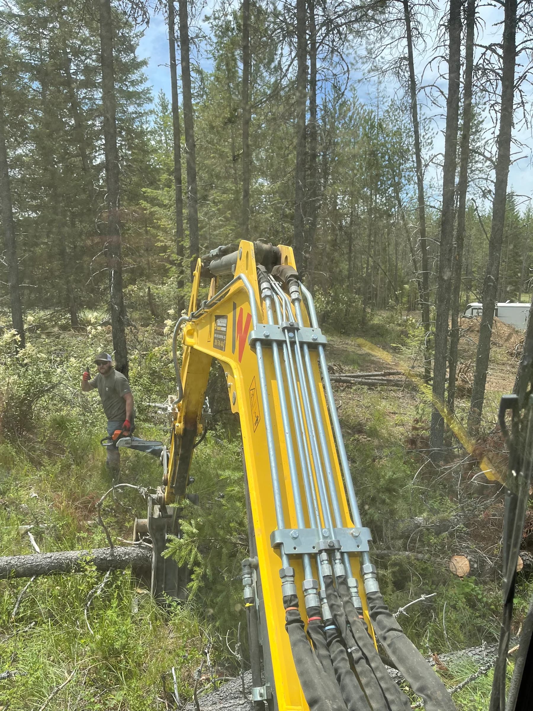 View past an excavator boom toward work among trees